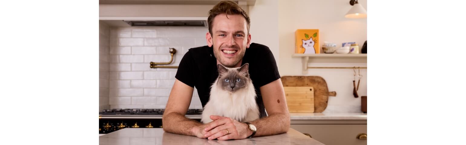 Rory the vet in a black shirt with a Ragdoll cat on a kitchen counter.